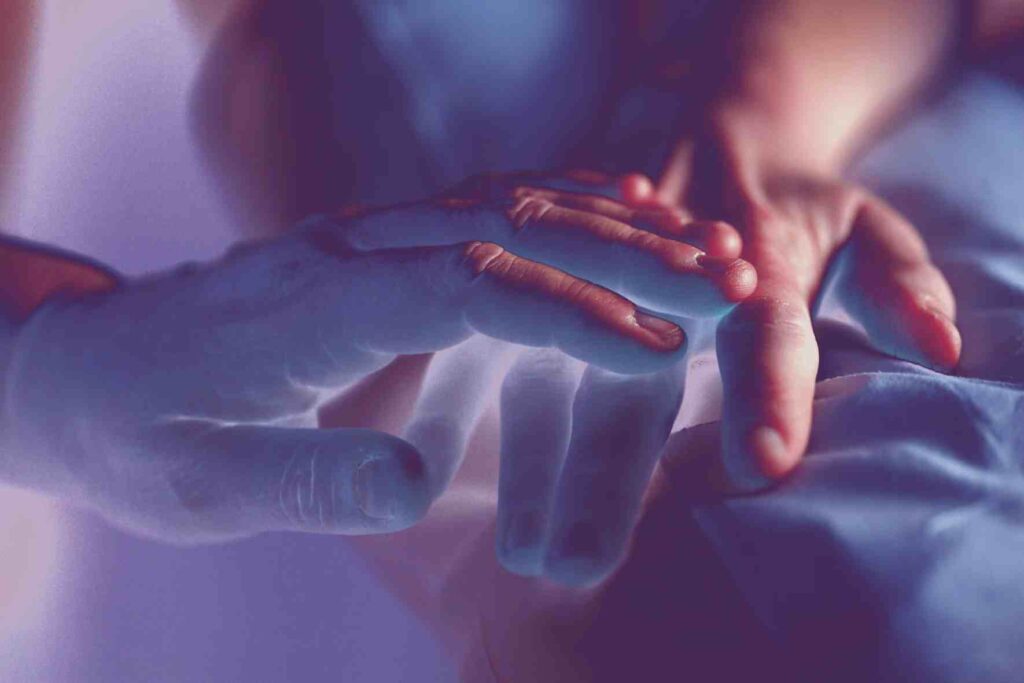 Une main bleu tient doucement la main d'une personne allongée sur un lit.